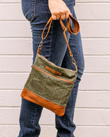 A woman holding a green and tan Tradevia Ellis River Crossbody Bag.