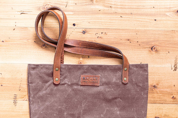 A durable, brown waxed canvas Allagash River Tote Bag on a wooden floor by Tradevia.