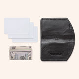 A black Tradevia Chamberlain Belt and Minimalist Wallet Bundle with a dollar bill and a credit card.