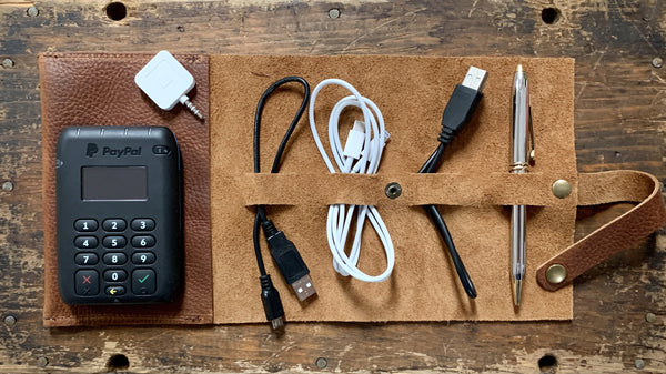 A top-grain leather Tradevia Leather Tech Organizer with a cell phone and cables.