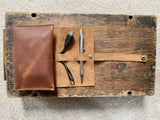 A pen case and pencils on a wood surface, next to a top-grain leather Tradevia Leather Tech Organizer.