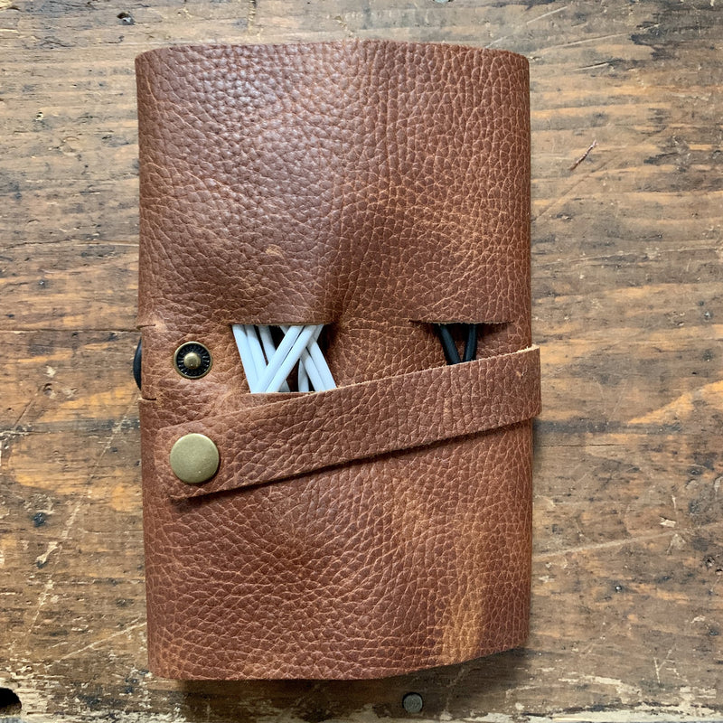 A brown Tradevia Leather Tech Organizer with cables attached to it.