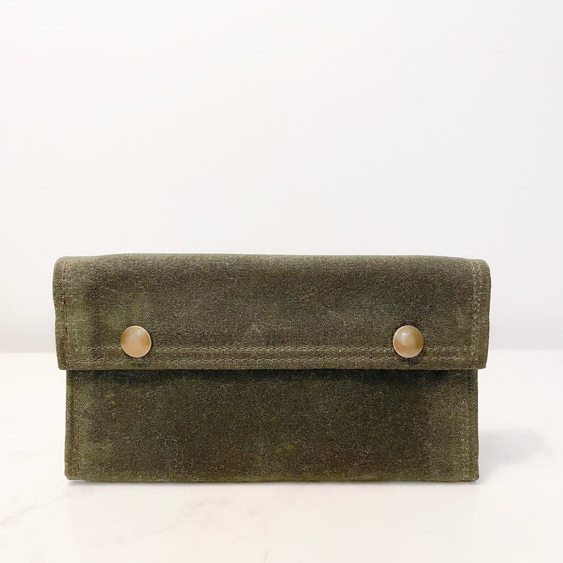 A green Tradevia waxed canvas bag with two buttons.