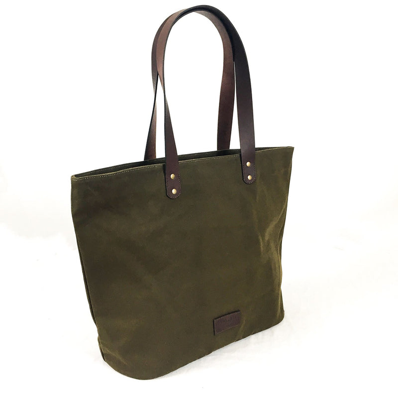 A green Tradevia waxed canvas tote bag with brown top-grain leather straps.