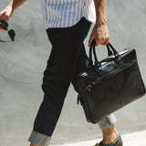 A man carrying a black West End Slim Leather Laptop Bag by Tradevia.