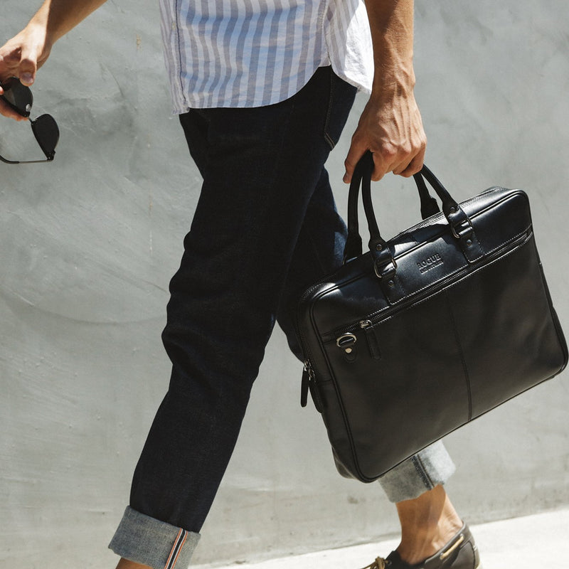 A man carrying a black West End Slim Leather Laptop Bag by Tradevia.