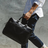 A man carrying a West End Slim Leather Laptop Bag by Tradevia with a removable strap.