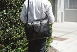 A person carrying a black West End Slim Leather Laptop Bag from Tradevia.