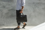 A man walking with a black, genuine leather West End Slim Laptop Bag by Tradevia.