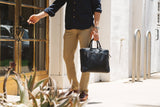 A man in a tan shirt holding a Tradevia West End Slim Leather Laptop Bag.